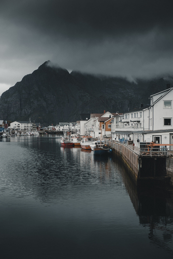 View of the traditional fishing village of Henningsvaer with colorful wooden houses and boats docked along the pier under a dramatic cloudy sky in Henningsvaer Nordland Norway. View of the traditional fishing village of Henningsvaer with colorful wooden houses and boats docked along the pier under a dramatic cloudy sky in Henningsvaer Nordland Norway.