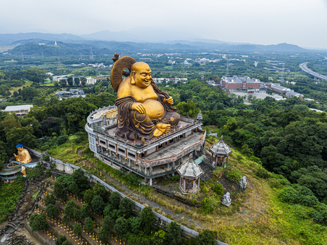 Aerial view of a large golden Buddha statue overlooking the lush green landscape and surrounding temple grounds in Jiuru Township Pingtung County Taiwan. Aerial view of a large golden Buddha statue overlooking the lush green landscape and surrounding temple grounds in Jiuru Township Pingtung County Taiwan.