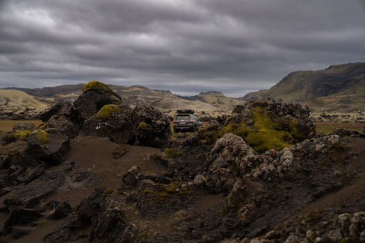 View of a rugged landscape with moss covered rocks under a cloudy sky with a vehicle in the distance Skaftárhreppur Iceland. View of a rugged landscape with moss covered rocks under a cloudy sky with a vehicle in the distance Skaftárhreppur Iceland.