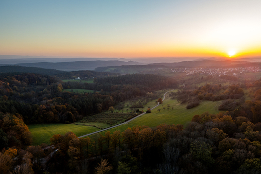 Aerial view of the Heuberger Tor area with rolling hills autumn forests and a winding road under a golden sunset in Tubingen Baden Wurttemberg Germany.