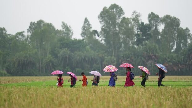 View of children walking with umbrellas through a field Bangladesh.