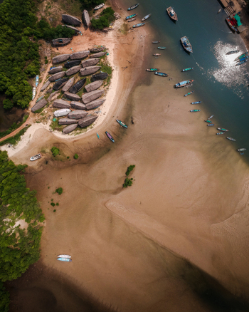 Aerial view of numerous fishing boats docked on the sandy riverbank and in the water surrounded by lush green vegetation in Vengurla Maharashtra India. Aerial view of numerous fishing boats docked on the sandy riverbank and in the water surrounded by lush green vegetation in Vengurla Maharashtra India.