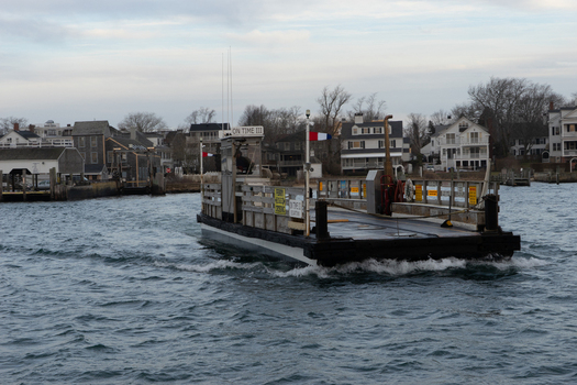 View of the On Time III ferry crossing the water towards the historic waterfront houses under an overcast sky in Edgartown Massachusetts United States.