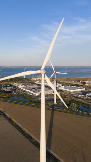 Aerial view of a large wind turbine standing near an industrial complex and data center facility with coastal waters and agricultural fields in Eemshaven Groningen Netherlands.