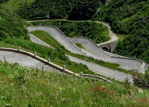 View of the historic Tremola road at Sankt Gotthard Pass with its iconic cobblestone serpentines winding through lush green alpine slopes Airolo Ticino Switzerland.