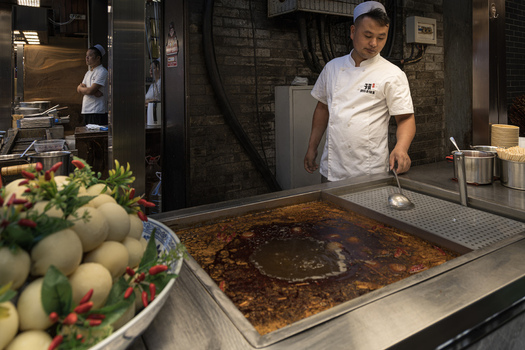 Xi an China 14 September 2026 View of a chef preparing a spicy hot pot in a restaurant kitchen with a large bowl of ingredients in the foreground.