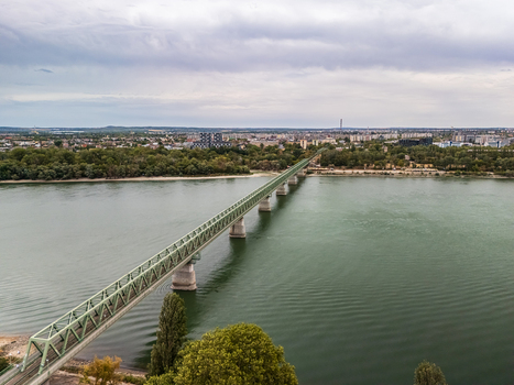 Aerial view of a green steel railway bridge crossing the Danube beside tree lined Nepsziget with urban neighborhoods and riverside greenery in Budapest Hungary. Aerial view of a green steel railway bridge crossing the Danube beside tree lined Nepsziget with urban neighborhoods and riverside greenery in Budapest Hungary.