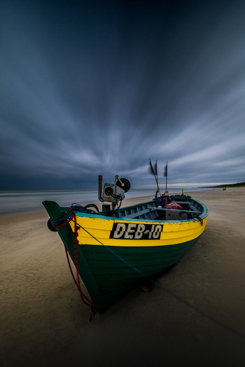 View of a colorful green and yellow fishing boat resting on a sandy beach under a dramatic cloudy sky in Debki Pomeranian Voivodeship Poland. View of a colorful green and yellow fishing boat resting on a sandy beach under a dramatic cloudy sky in Debki Pomeranian Voivodeship Poland.