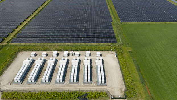 Aerial view of a large solar farm featuring rows of photovoltaic panels and white battery storage units situated in a rural landscape in Wanneperveen Overijssel Netherlands.