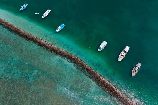 Aerial view of several boats moored along a stone breakwater in the turquoise waters of the Indian Ocean in Kulhudhuffushi Haa Dhaalu Atoll Maldives. Aerial view of several boats moored along a stone breakwater in the turquoise waters of the Indian Ocean in Kulhudhuffushi Haa Dhaalu Atoll Maldives.