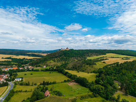 Aerial view of Tocnik Castle perched on a forested hill surrounded by green fields and rural houses under a blue sky in Tocnik Stredocesky kraj Czechia. Aerial view of Tocnik Castle perched on a forested hill surrounded by green fields and rural houses under a blue sky in Tocnik Stredocesky kraj Czechia.