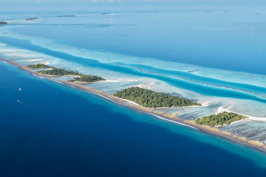 Aerial view of lush tropical islands with green palm trees and turquoise coral reefs surrounded by the deep blue ocean under a clear sky near Vaanee Dhaalu Atoll Maldives. Aerial view of lush tropical islands with green palm trees and turquoise coral reefs surrounded by the deep blue ocean under a clear sky near Vaanee Dhaalu Atoll Maldives.