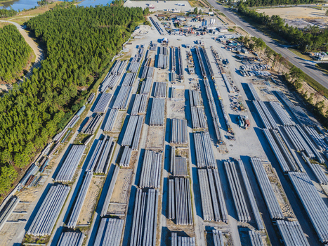 Aerial view of an industrial concrete bridge manufacturing facility with rows of steel I beams heavy machinery and storage yards in Wilmington North Carolina United States. Aerial view of an industrial concrete bridge manufacturing facility with rows of steel I beams heavy machinery and storage yards in Wilmington North Carolina United States.
