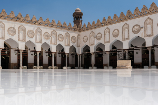 View of Al Azhar Mosque featuring the white marble courtyard reflecting the arches intricate stone carvings and a minaret under a clear blue sky Cairo Egypt. View of Al Azhar Mosque featuring the white marble courtyard reflecting the arches intricate stone carvings and a minaret under a clear blue sky Cairo Egypt.