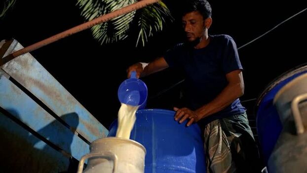 View of a man pouring milk into a churn at night in Bangladesh. View of a man pouring milk into a churn at night in Bangladesh.