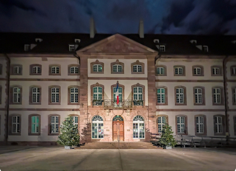 View of the historic Unterlinden Museum building illuminated at night with Christmas trees and a French flag on the balcony in Colmar Grand Est France.