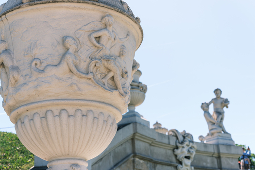 View of an ornate stone urn with mythological relief carvings and garden sculptures under a clear blue sky in Vienna Austria. View of an ornate stone urn with mythological relief carvings and garden sculptures under a clear blue sky in Vienna Austria.