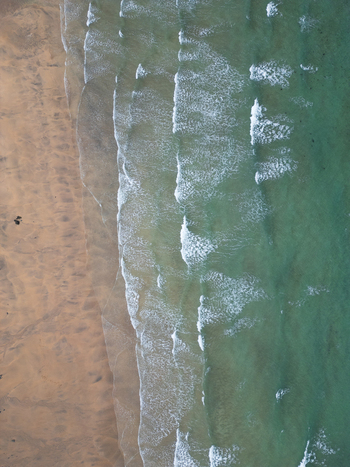 Aerial view of waves rolling onto the sandy shore of Godrevy Beach with turquoise water and white foam in Gwithian England United Kingdom. Aerial view of waves rolling onto the sandy shore of Godrevy Beach with turquoise water and white foam in Gwithian England United Kingdom.