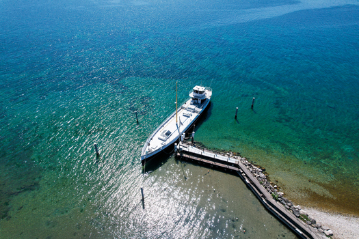 Aerial view of a white boat moored at a wooden pier on the turquoise waters of Lake Geneva Perroy Vaud Switzerland. Aerial view of a white boat moored at a wooden pier on the turquoise waters of Lake Geneva Perroy Vaud Switzerland.