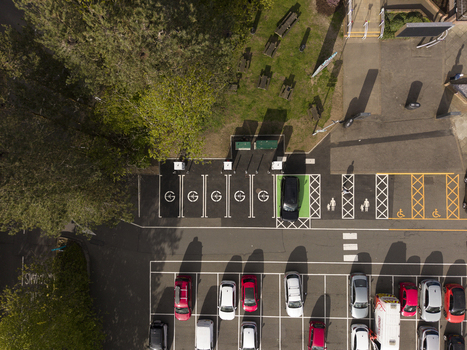 04 May 2026 Aerial view of a parking lot featuring electric vehicle charging points designated parking bays and a person walking near a green area with picnic tables. 04 May 2026 Aerial view of a parking lot featuring electric vehicle charging points designated parking bays and a person walking near a green area with picnic tables.