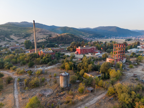 Aerial view of an abandoned industrial complex with a tall chimney red brick buildings and a skeletal structure set amidst trees and rolling hills in Velingrad Pazardzhik Bulgaria. Aerial view of an abandoned industrial complex with a tall chimney red brick buildings and a skeletal structure set amidst trees and rolling hills in Velingrad Pazardzhik Bulgaria.