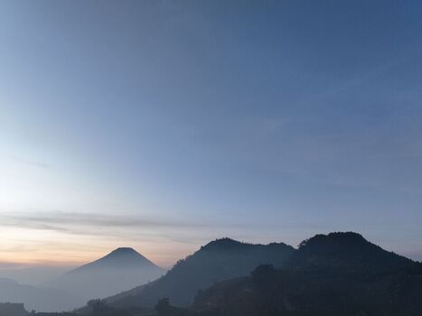 Aerial view of the Dieng volcanic plateau mountains at sunrise with soft golden light and misty atmosphere in Kejajar Central Java Indonesia. Aerial view of the Dieng volcanic plateau mountains at sunrise with soft golden light and misty atmosphere in Kejajar Central Java Indonesia.