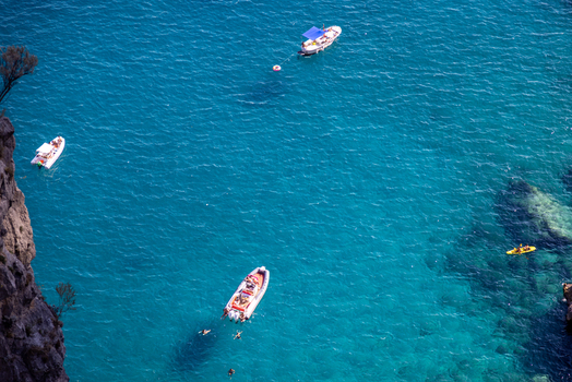 Aerial view of boats and a kayak floating in the clear turquoise waters near the rocky cliffs of Capri Campania Italy. Aerial view of boats and a kayak floating in the clear turquoise waters near the rocky cliffs of Capri Campania Italy.