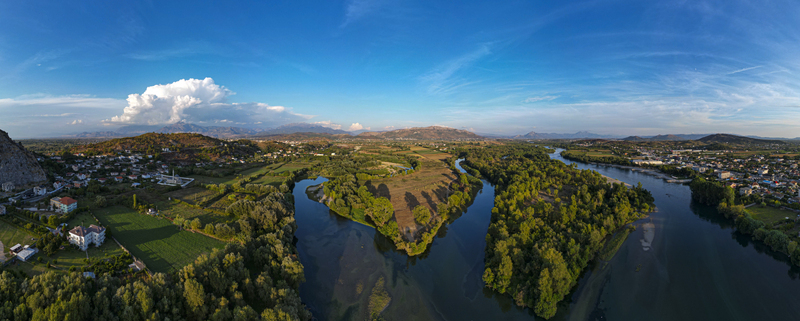 Aerial view of the confluence of the Drin and Buna rivers near Shkoder featuring lush green riverbanks surrounding hills and a clear blue sky in Shkoder Shkoder County Albania.