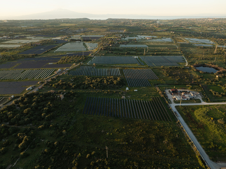 Aerial view of a large solar panel farm surrounded by green fields and trees with Mount Etna visible in the distance Augusta Sicily Italy. Aerial view of a large solar panel farm surrounded by green fields and trees with Mount Etna visible in the distance Augusta Sicily Italy.