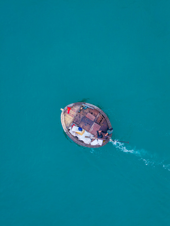 Aerial view of a traditional round basket boat with a person rowing across the turquoise water in Vietnam. Aerial view of a traditional round basket boat with a person rowing across the turquoise water in Vietnam.