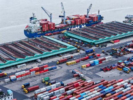 Aerial view of Chattogram Port with a large cargo ship docked at the pier rows of colorful shipping containers and trucks in the busy terminal in Chittagong Chittagong Division Bangladesh.