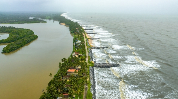Aerial view of Mattu Beach with a narrow strip of land separating backwaters from the Arabian Sea featuring palm trees and stone breakwaters in Udupi Karnataka India.