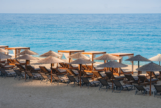 View of the beach with sun loungers under thatched umbrellas contrasting against the turquoise water Kathisma beach Lefkada Greece. View of the beach with sun loungers under thatched umbrellas contrasting against the turquoise water Kathisma beach Lefkada Greece.