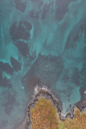 Aerial view of the rugged coastline of Senja with turquoise waters dark rocky cliffs and patches of autumn colored vegetation in Senja Troms Norway.