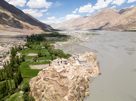 Aerial view of Charasa Gonpa monastery perched on a rocky outcrop overlooking the wide river valley with lush green fields and arid mountains in the background in Charasa Ladakh India.