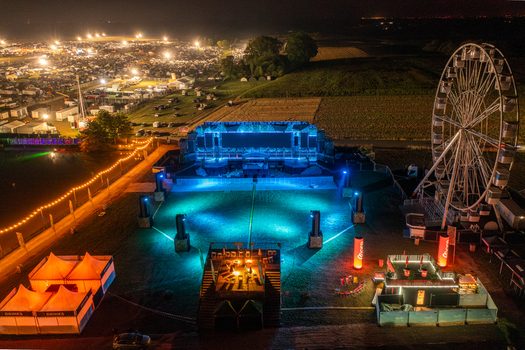 Herzogenaurach Germany 25 July 2025 Aerial view of Open Beatz Festival featuring the main stage with blue lights a Ferris wheel and a vast camping area at night. Herzogenaurach Germany 25 July 2025 Aerial view of Open Beatz Festival featuring the main stage with blue lights a Ferris wheel and a vast camping area at night.