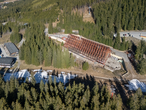 Aerial view of a large building under construction with a steel frame roof surrounded by dense pine forests and patches of melting snow Demanovska Dolina Zilina Region Slovakia.
