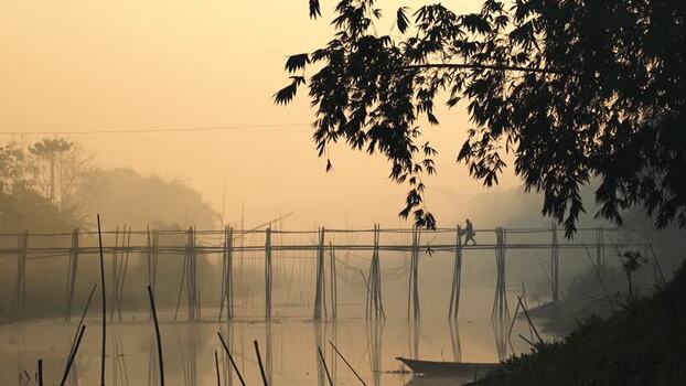 View of a person walking on a bamboo bridge at dawn Bangladesh.