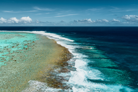 Aerial view of the Aitutaki coral reef with turquoise lagoon waters breaking waves and deep blue ocean under a clear sky in Cook Islands. Aerial view of the Aitutaki coral reef with turquoise lagoon waters breaking waves and deep blue ocean under a clear sky in Cook Islands.