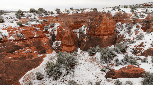 Aerial view of red rock formations and desert vegetation covered in fresh snow under a cloudy sky in Page Arizona United States.