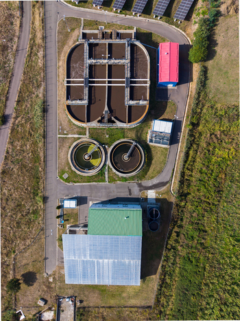 Aerial view of the sewage treatment plant featuring circular sedimentation tanks and industrial buildings surrounded by green fields in Targu Secuiesc Covasna County Romania.