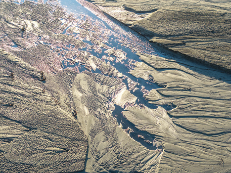 Aerial view of intricate sand patterns and a water channel flowing through a coastal landscape in Poland. Aerial view of intricate sand patterns and a water channel flowing through a coastal landscape in Poland.