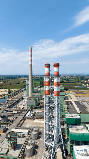Aerial view of a combined cycle natural gas power station featuring tall chimneys and industrial infrastructure surrounded by fields in Tavazzano con Villavesco Lombardy Italy.