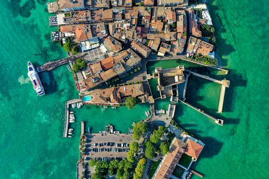 Aerial view of Castello Scaligero di Sirmione a historic fortress surrounded by the turquoise waters of Lake Garda and terracotta rooftops in Sirmione Lombardia Italy.