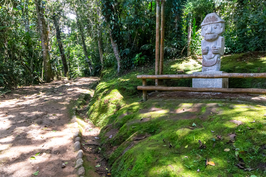 View of a pre Columbian stone statue standing beside a dirt path in the lush mossy forest of San Agustin Archaeological Park San Agustin Huila Colombia.