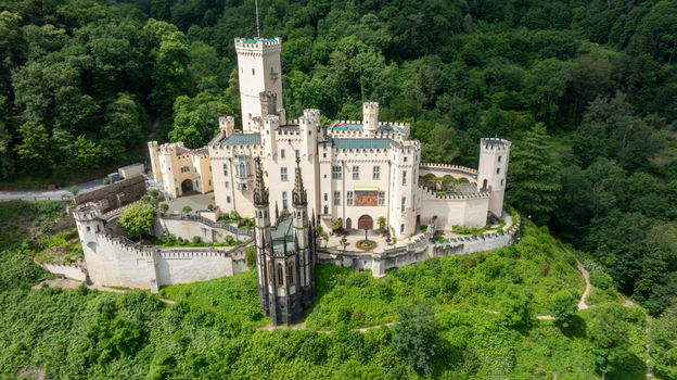 Aerial view of Stolzenfels Castle featuring its white towers and gothic revival architecture surrounded by lush green forest on a hill in Koblenz Rheinland Pfalz Germany. Aerial view of Stolzenfels Castle featuring its white towers and gothic revival architecture surrounded by lush green forest on a hill in Koblenz Rheinland Pfalz Germany.