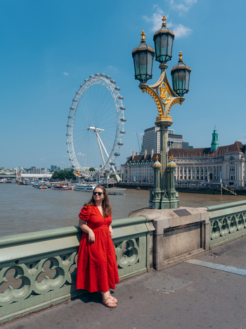 View of a vibrant red dressed woman leaning on an ornate green bridge with the majestic London Eye soaring under a clear sky London England United Kingdom. View of a vibrant red dressed woman leaning on an ornate green bridge with the majestic London Eye soaring under a clear sky London England United Kingdom.