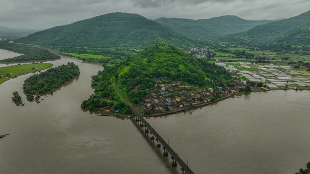 Aerial view of the Mumbai Goa Highway bridge crossing a river near a village on a hill surrounded by lush green landscapes and agricultural fields in Mahad Maharashtra India.