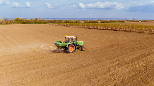 Aerial view of a tractor meticulously spreading fertilizer across the vast expanse of a field creating a stark contrast with the sky Sremska Mitrovica Vojvodina Serbia. Aerial view of a tractor meticulously spreading fertilizer across the vast expanse of a field creating a stark contrast with the sky Sremska Mitrovica Vojvodina Serbia.