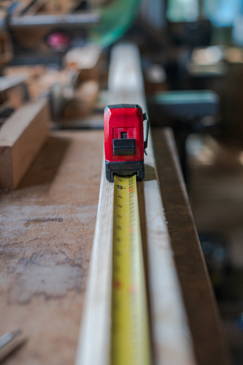 View of a red tape measure extended along a piece of timber in a workshop in Looe Cornwall United Kingdom. View of a red tape measure extended along a piece of timber in a workshop in Looe Cornwall United Kingdom.